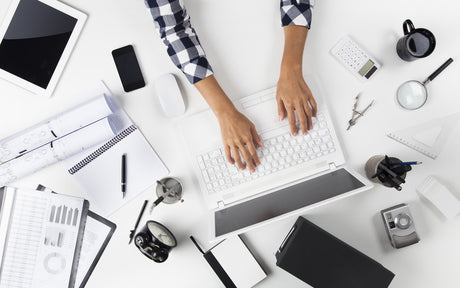 Crowded office desk with someone writing at laptop